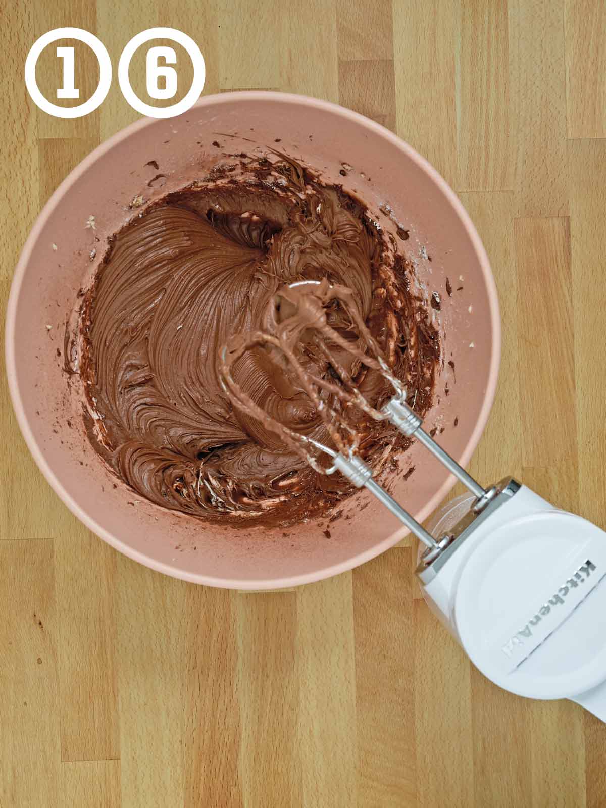 A bowl of chocolate frosting with a mixer.