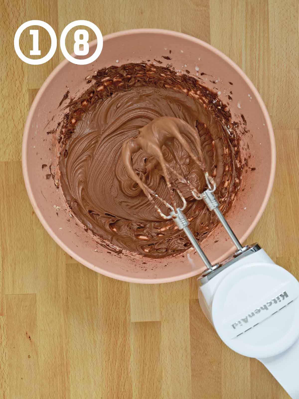 A bowl of chocolate frosting with a mixer in it.