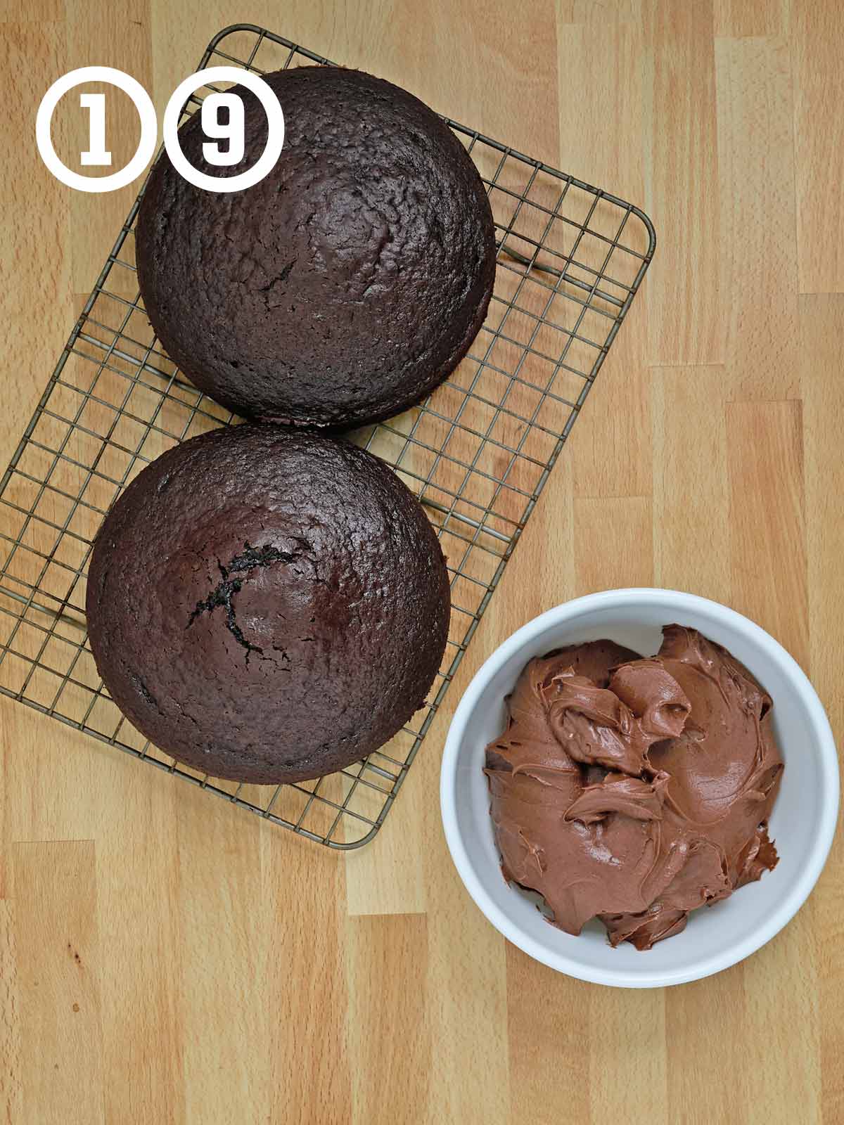 Two Guinness chocolate cakes on a cooling rack next to a bowl of chocolate icing.