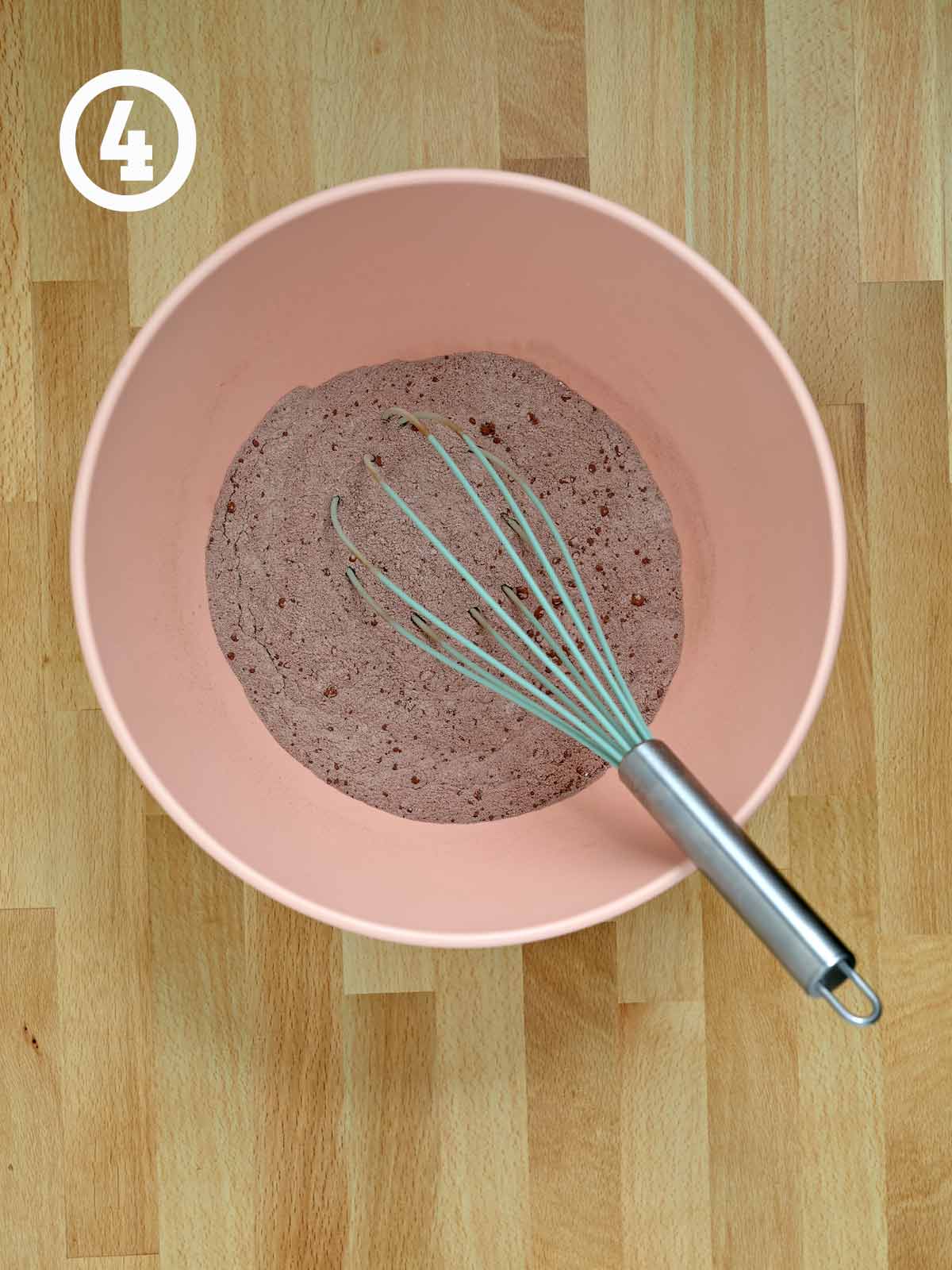 A pink bowl with a whisk and Guinness chocolate cake dry ingredients.