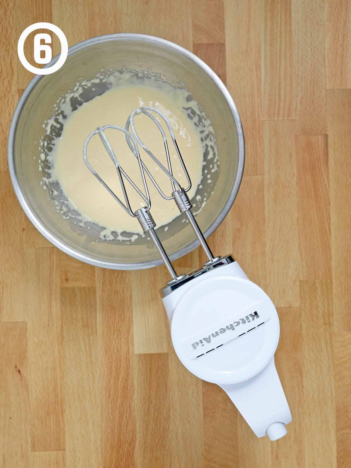 A bowl of batter with an electric mixer in it with wet ingredients.