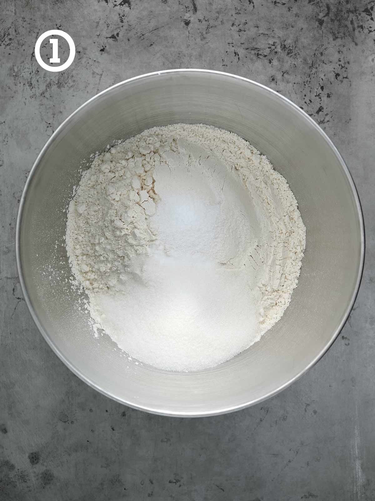 Flour sugar, salt, and baking soda in a bowl on a concrete surface.