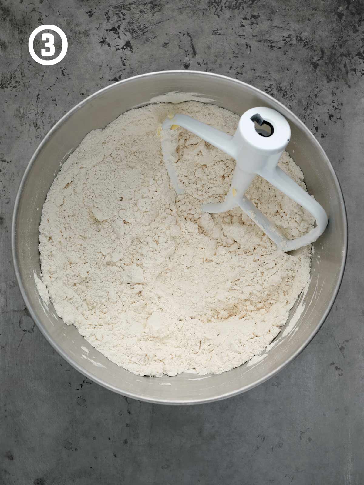 A metal mixing bowl with flour and butter mixture in it.