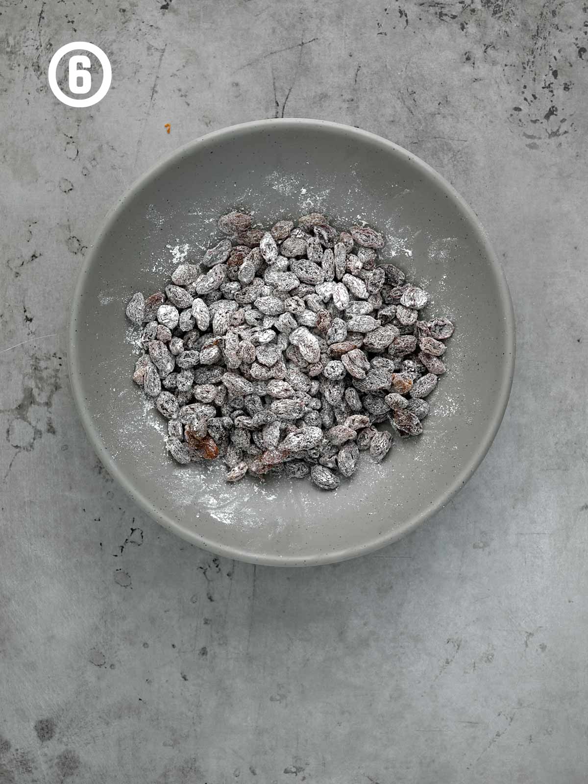 A bowl of floured raisins on a concrete surface.