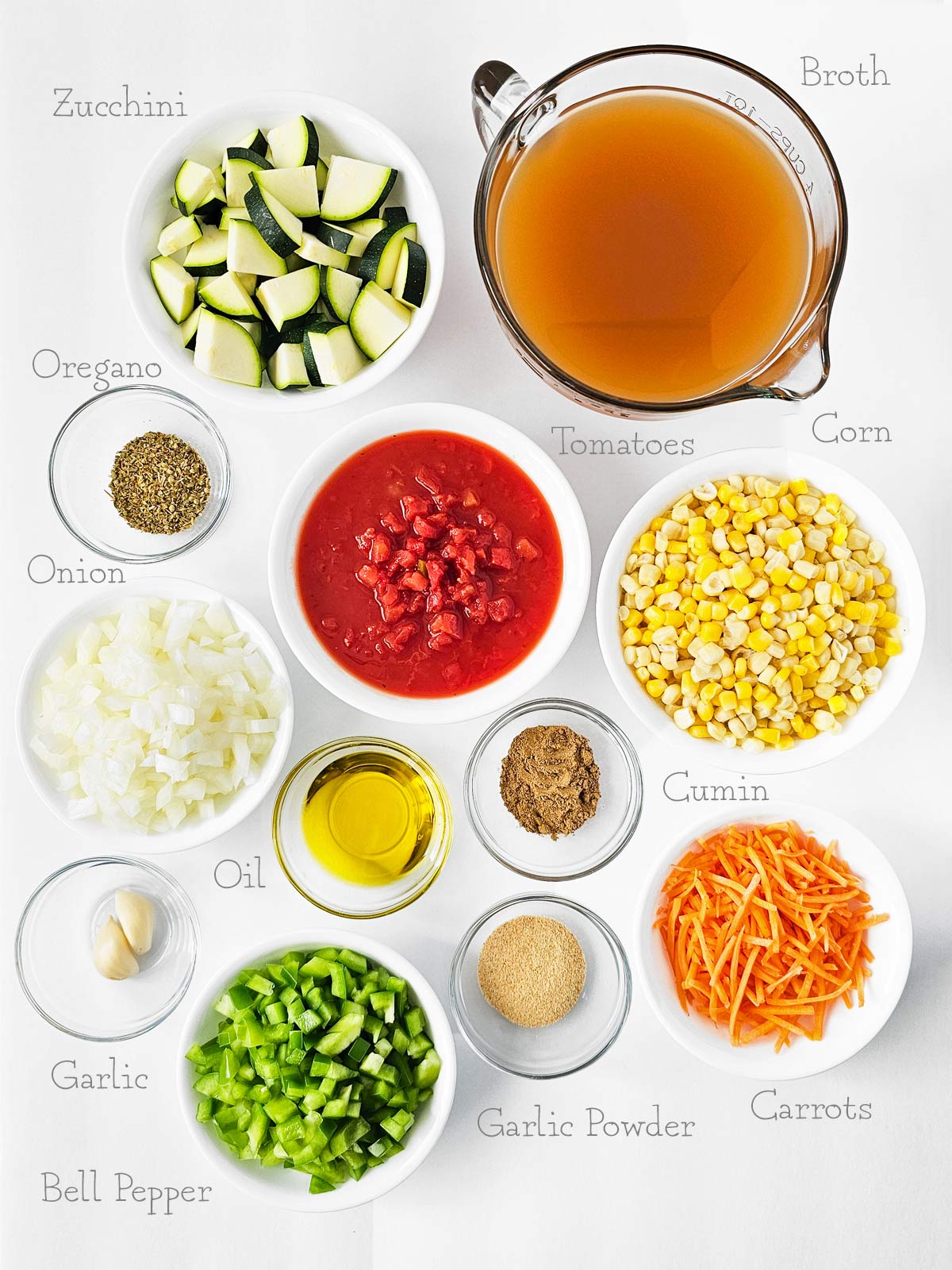 The ingredients for a vegetable soup are laid out on a white table.