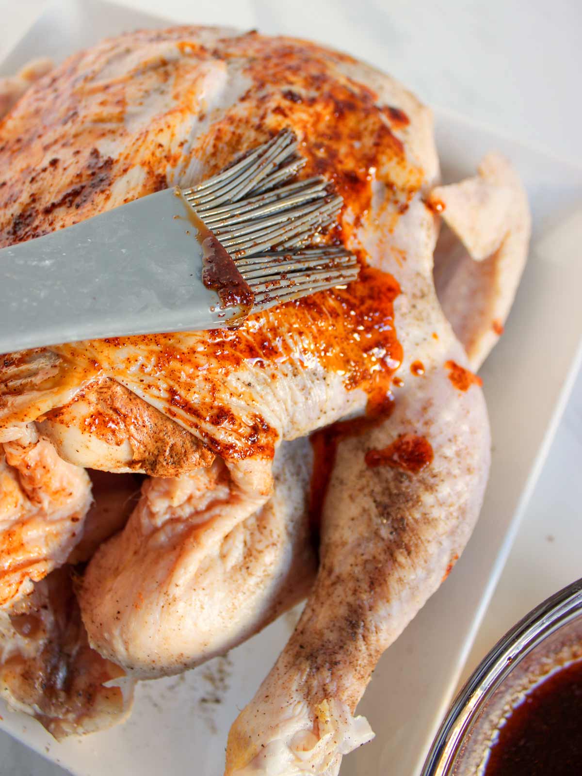 Chicken being basted with BBQ sauce.