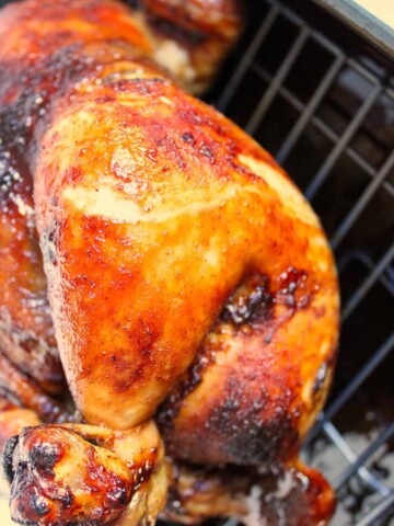 A roasted chicken sitting in a roasting pan, cooked with barbecue sauce.