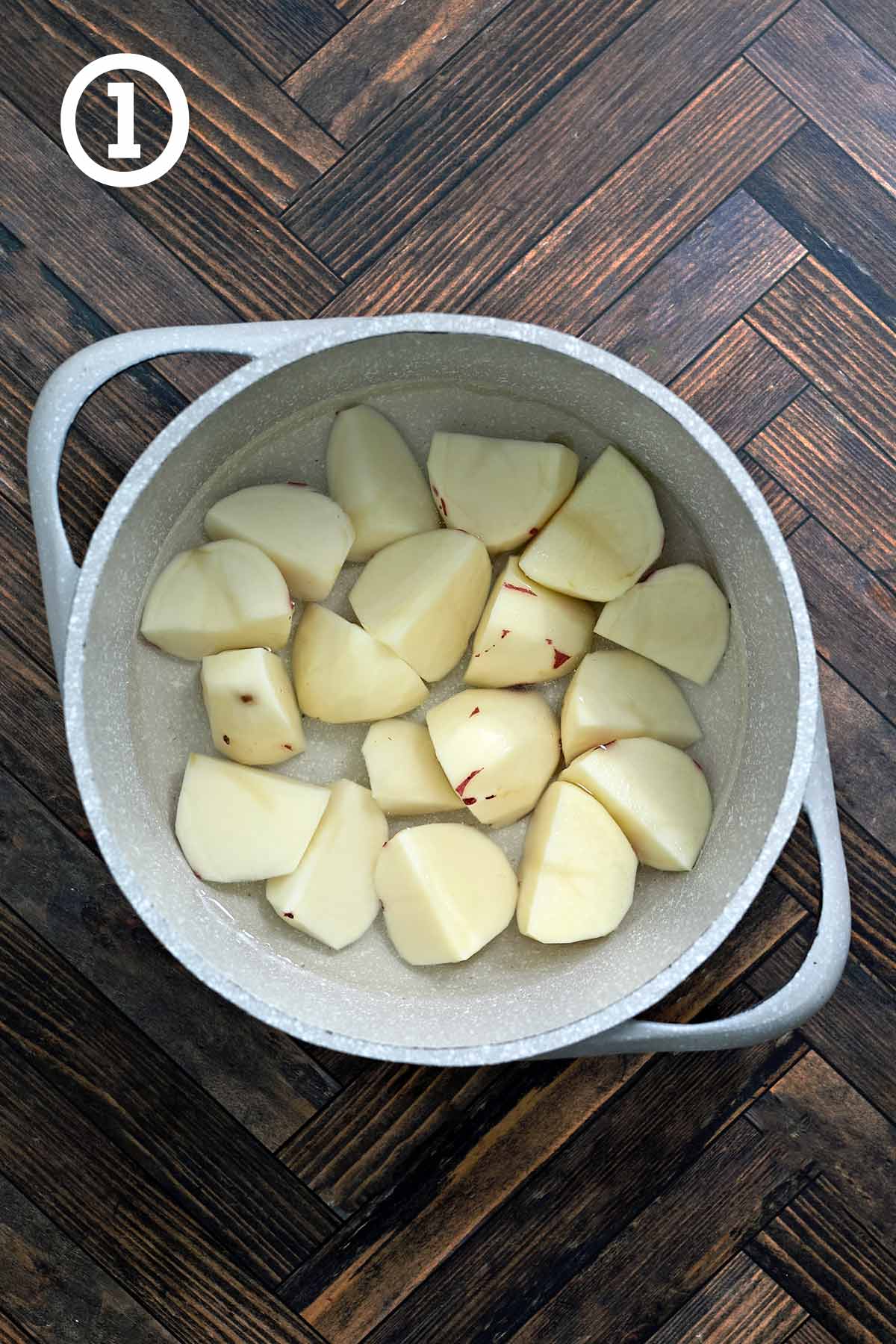 A pot of peeledand chopped red potatoes on a wood surface.