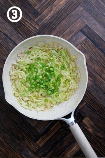 A frying pan with cabbage and added green onions.