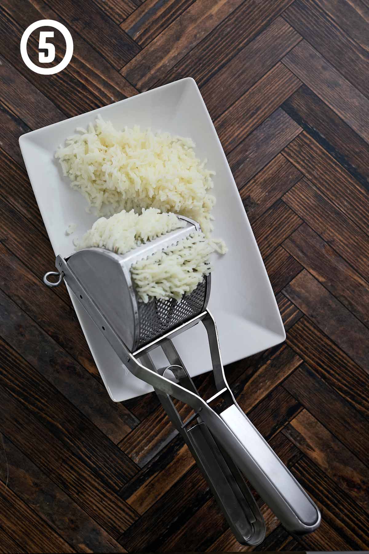 A plate with potato ricer and riced potatoes.