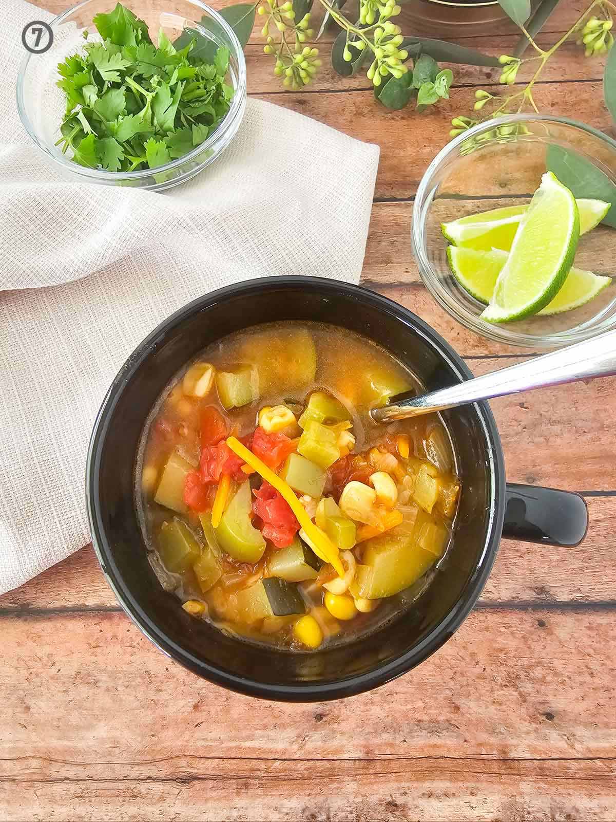 Vegetable soup with Mexican flair in a black bowl on a wooden table.
