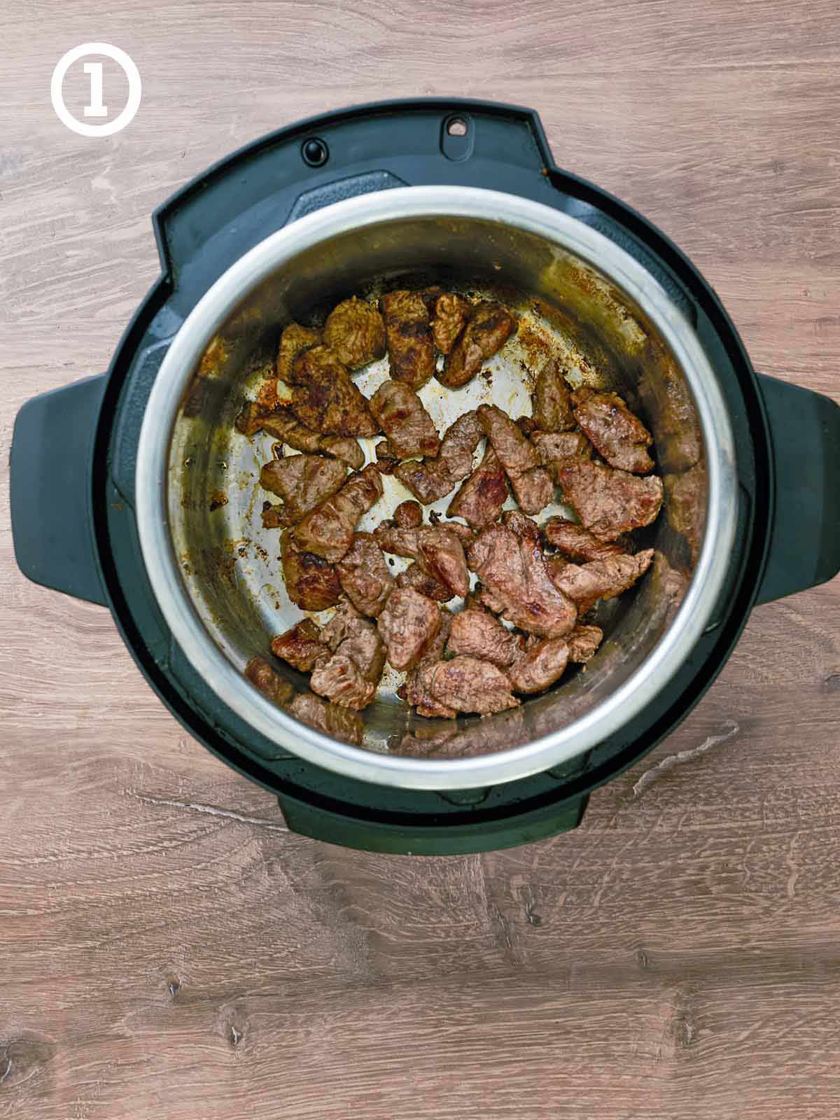 An instant pot with meat in it on a wooden table.