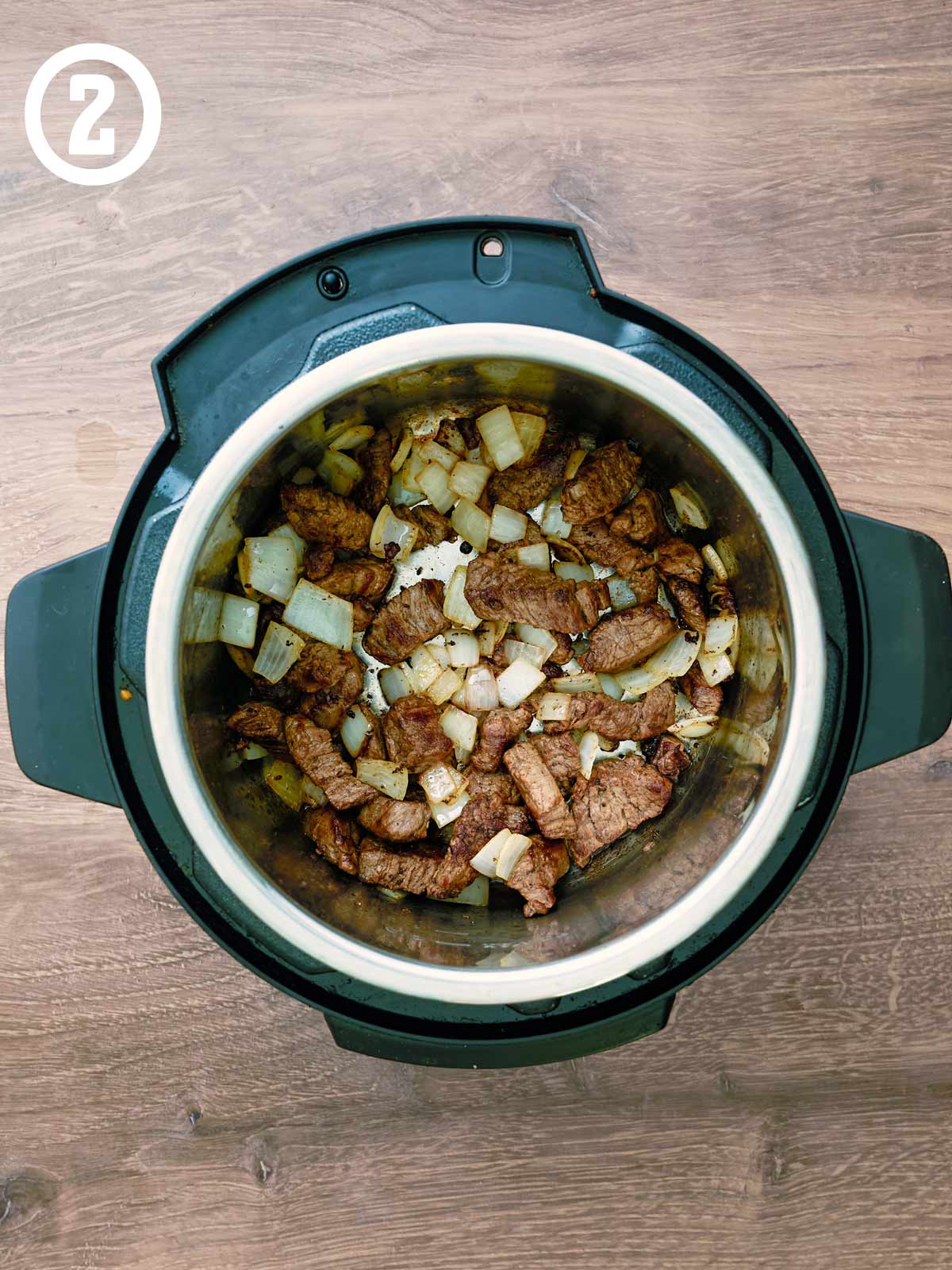 An instant pot filled with meat and onions.
