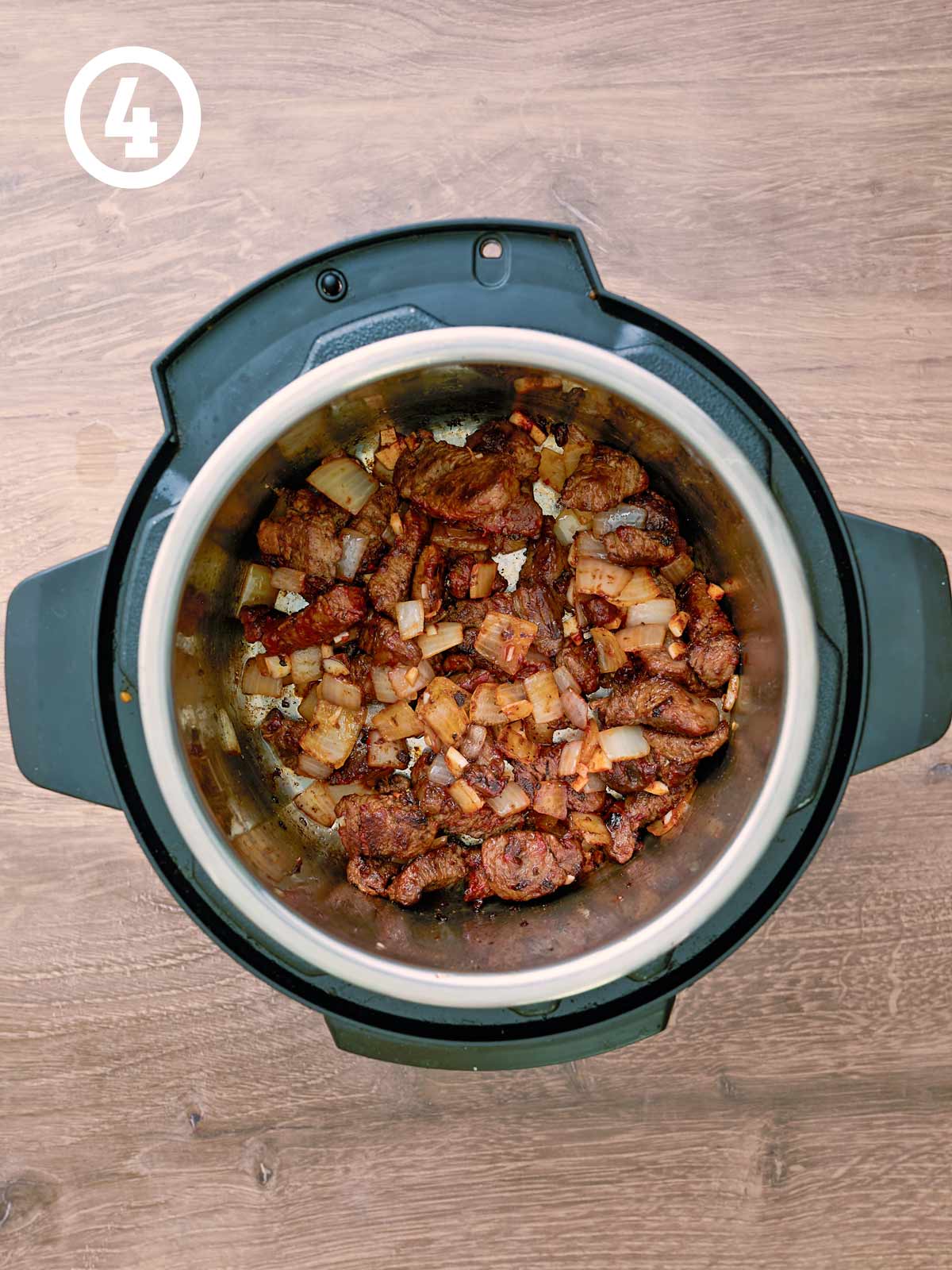 An instant pot filled with meat and onions on a wooden table.
