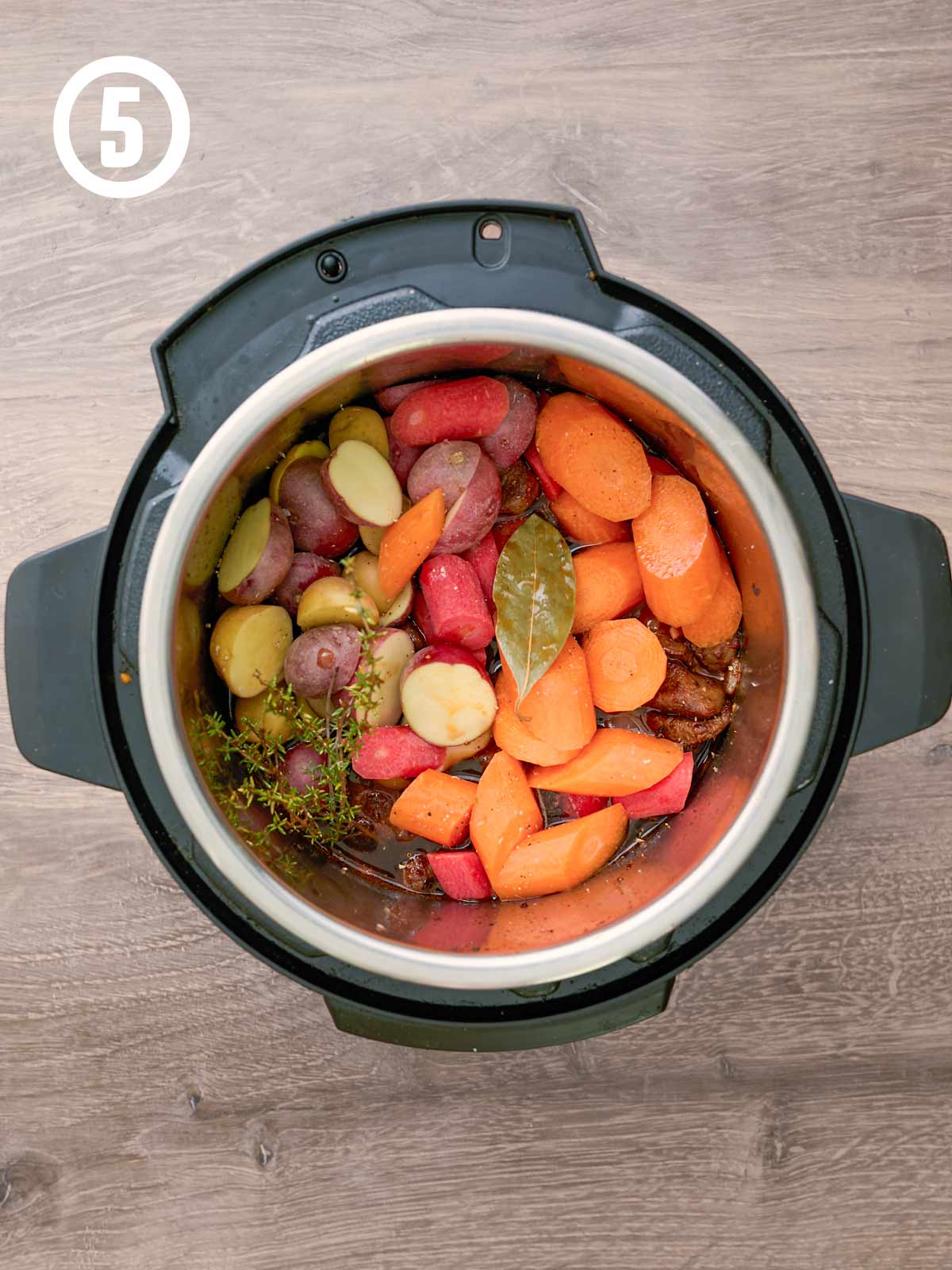 A slow cooker filled with cooked beef and raw carrots and potatoes.
