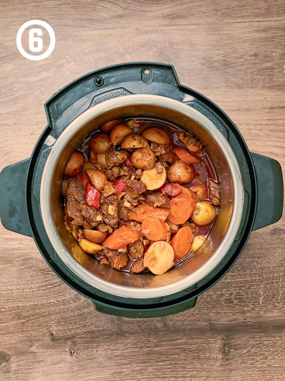 A slow cooker full of meat and vegetables on a wooden table.