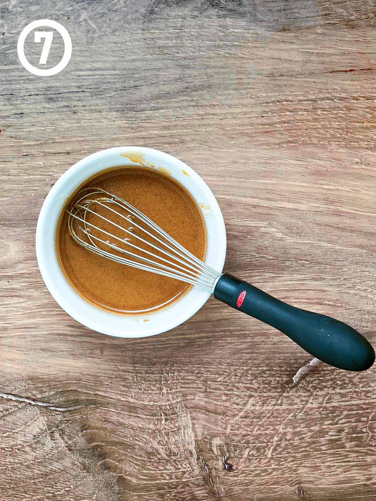 A bowl of sauce with a whisk in it.