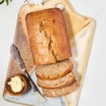 A loaf of sliced banana bread on a golden tray, accompanied by a small bowl of butter and a knife.