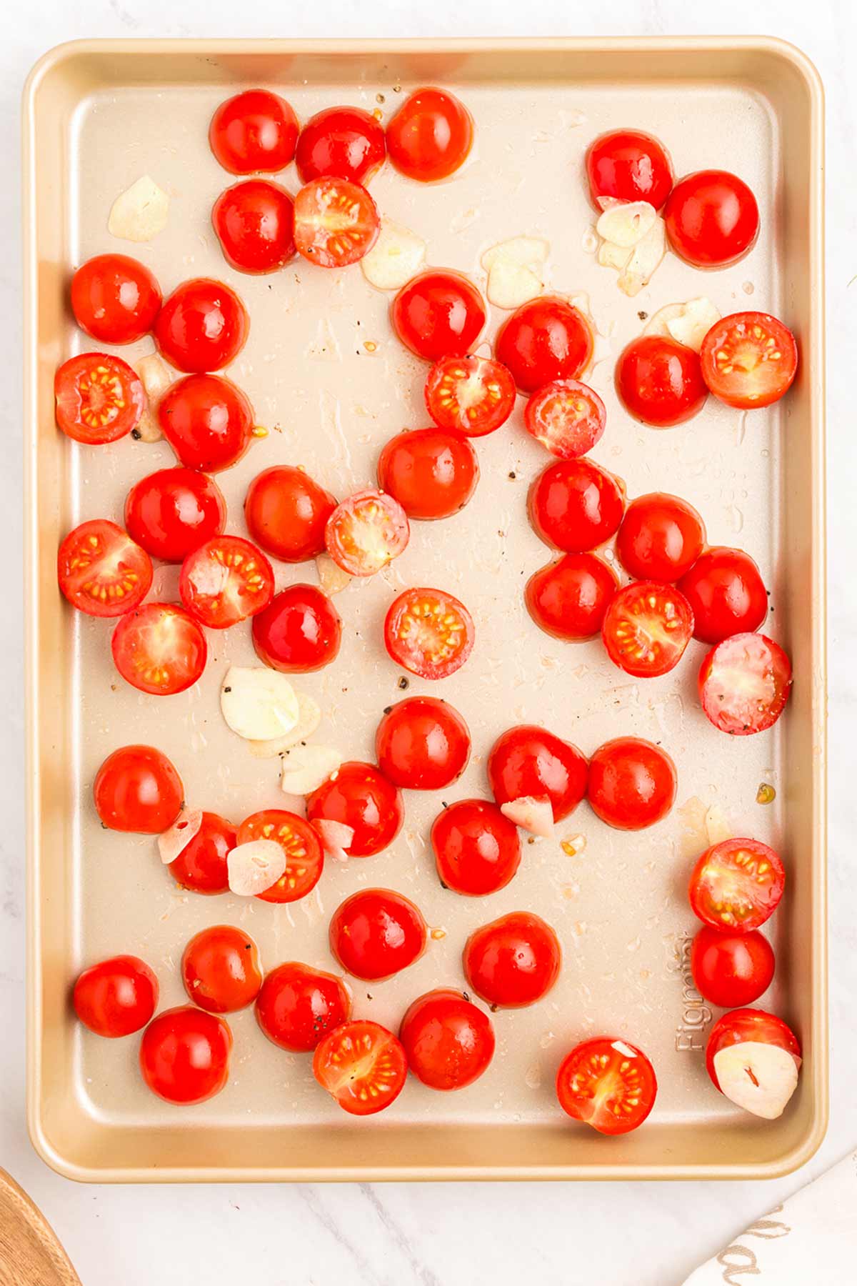 Cherry tomato halves and sliced garlic scattered on a baking sheet, ready for roasting.