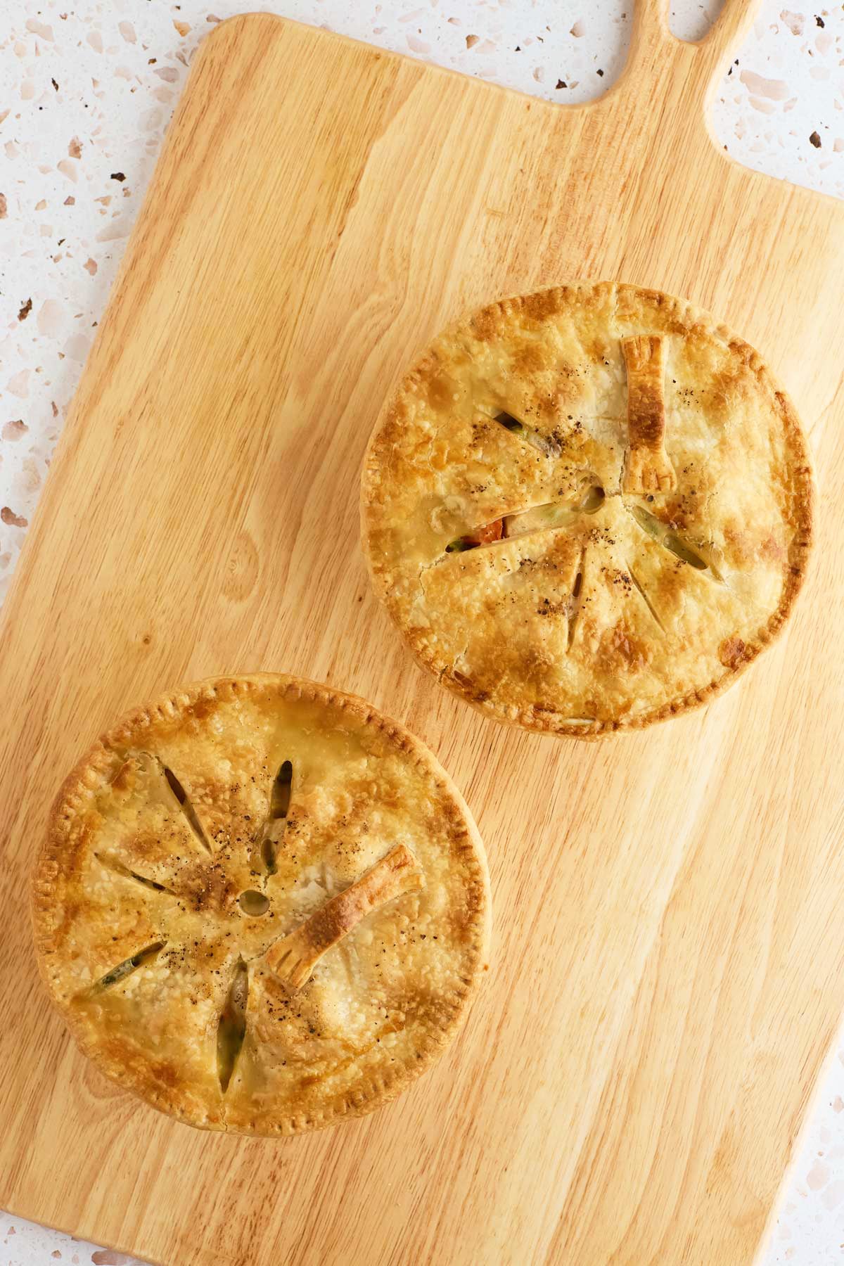 Two golden-brown pies with slits on top sit on a wooden cutting board.