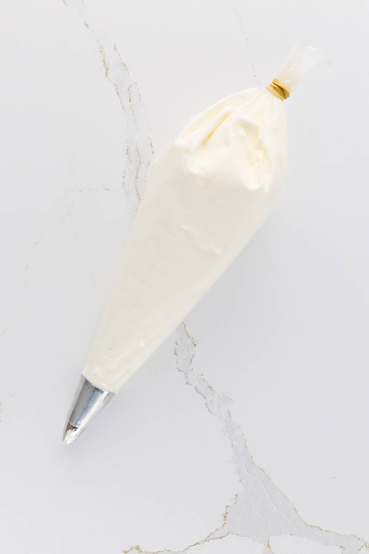 A piping bag filled with whipped cream, closed with a rubber band at the top, rests on a marble surface.