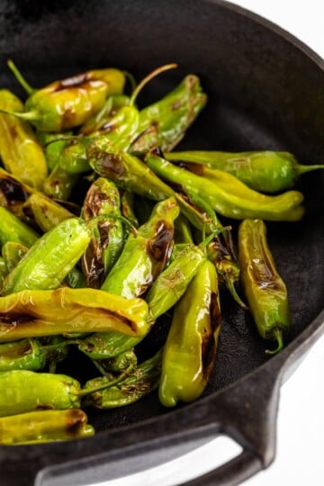 Blistered shishito peppers in a cast iron pan.