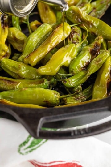 Pouring oil onto shishito peppers in a cast iron pan.