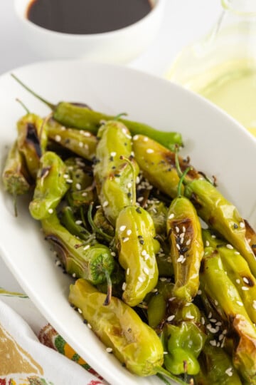 Shishito peppers on a serving platter with sesame seeds.