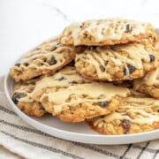 A plate of oatmeal cookies with raisins, topped with a light drizzle of icing, stacked on a white plate over a striped cloth.