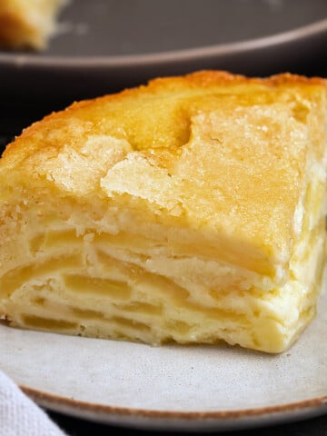 A slice of French Apple Cake sits on a plate next to a fork, showing visible apple slices and a golden-brown crust—an inviting taste of classic french apple cake recipes.
