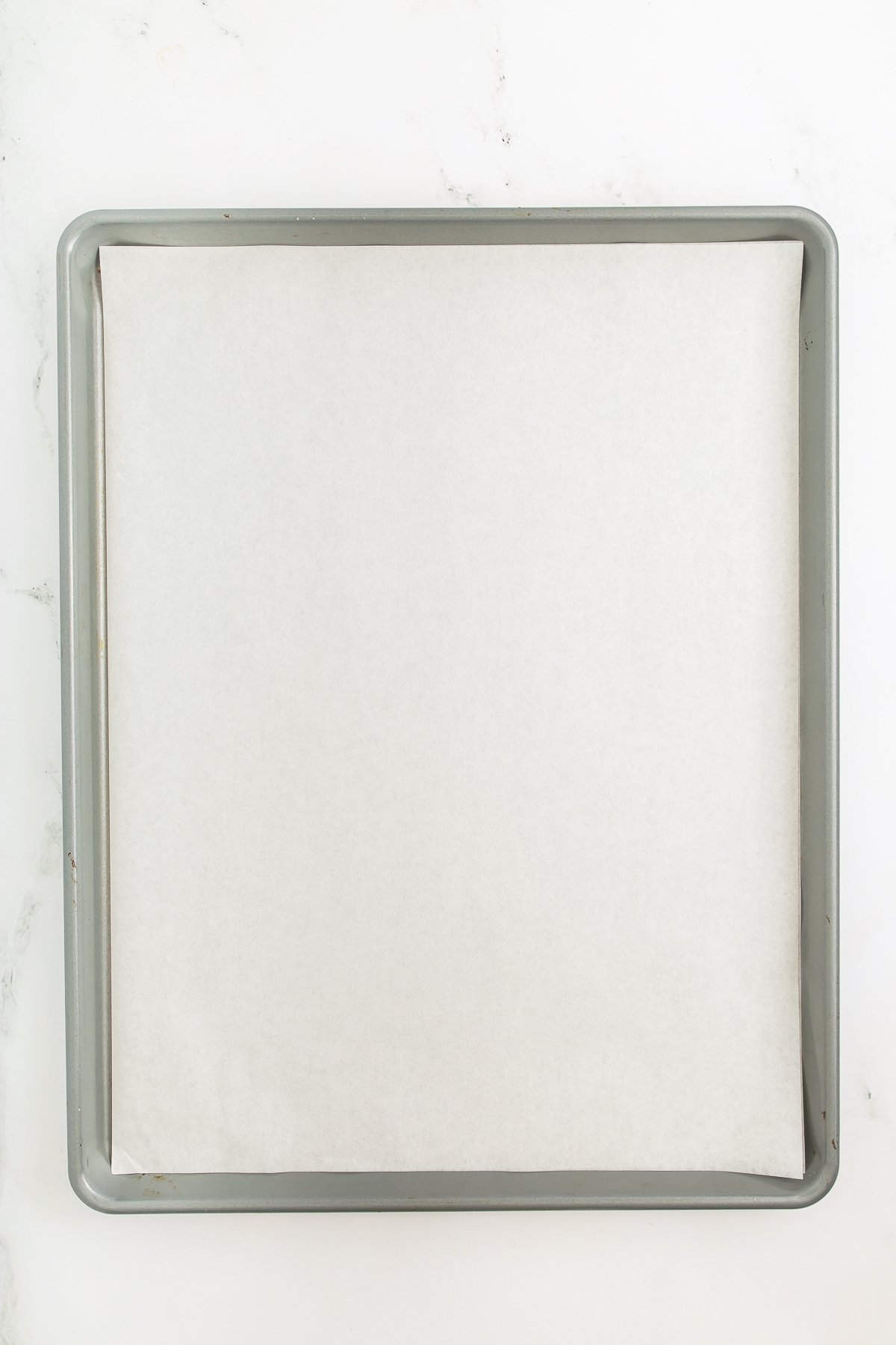A metal baking sheet lined with a sheet of white parchment paper on a white surface.