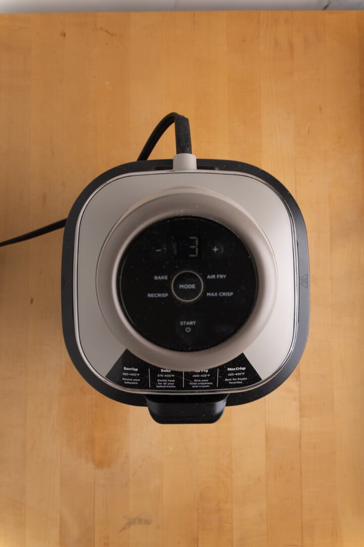 Top-down view of a black and silver air fryer on a wooden surface, showing its control panel and digital display with the number 3.