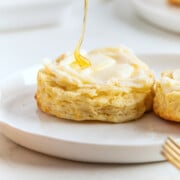 A biscuit with melted butter on a white plate, being drizzled with honey—freshly made air fryer biscuits for a warm and delicious treat.