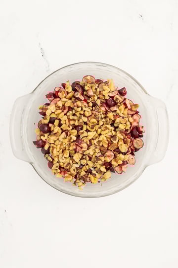 A glass bowl filled with chopped cherries and chopped nuts, viewed from above on a white surface.