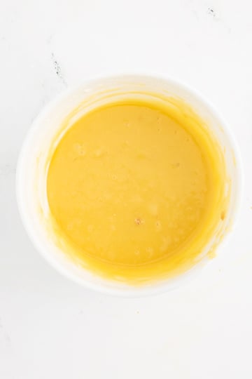 A white bowl filled with smooth yellow batter on a white surface.
