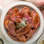 A bowl of roasted purple fingerling potatoes garnished with rosemary and sea salt, placed next to a pink napkin and a salt shaker.