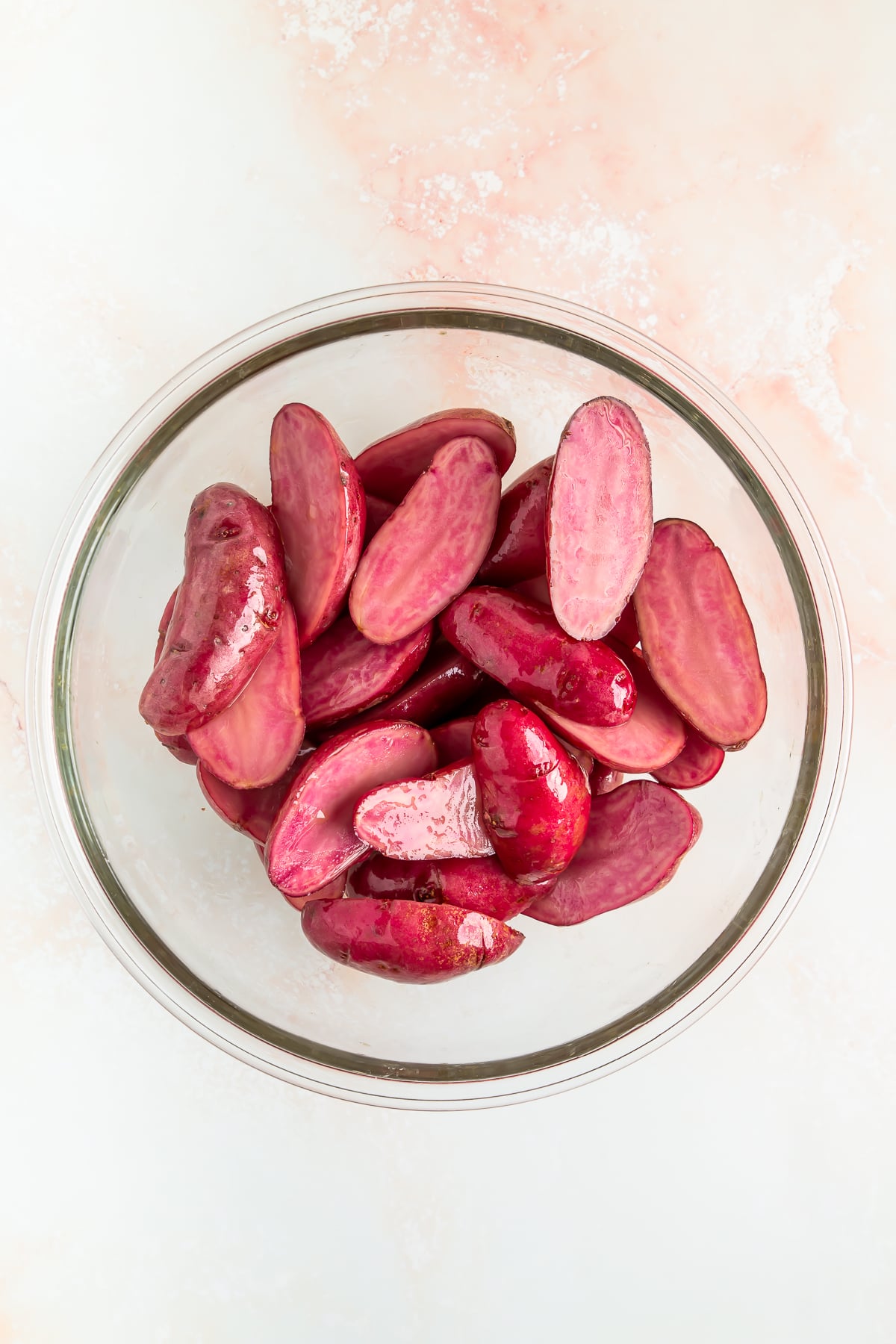 A glass bowl filled with sliced purple potatoes on a light-colored surface.