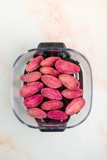 A glass baking dish filled with halved, uncooked purple potatoes arranged in a single layer on a light-colored surface.
