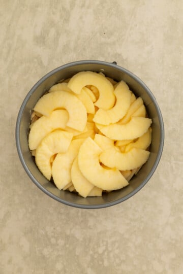 A round baking pan filled with evenly arranged slices of peeled apple on a light beige surface.