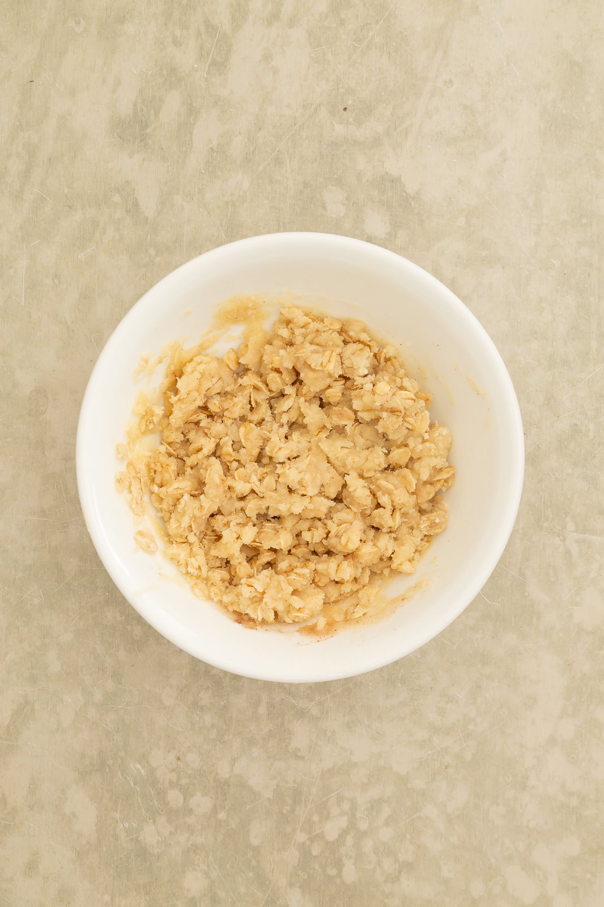 A white bowl filled with streusel sits on a light-colored textured surface.