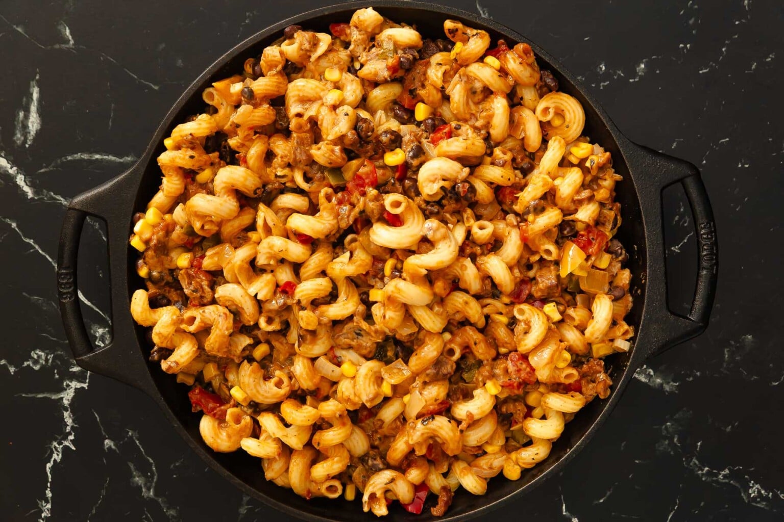 Cooked pasta with chorizo, corn, tomatoes, and sauce in a black pan on a dark marble surface—an inviting Mexican pasta recipe perfect for flavorful weeknight dinners.