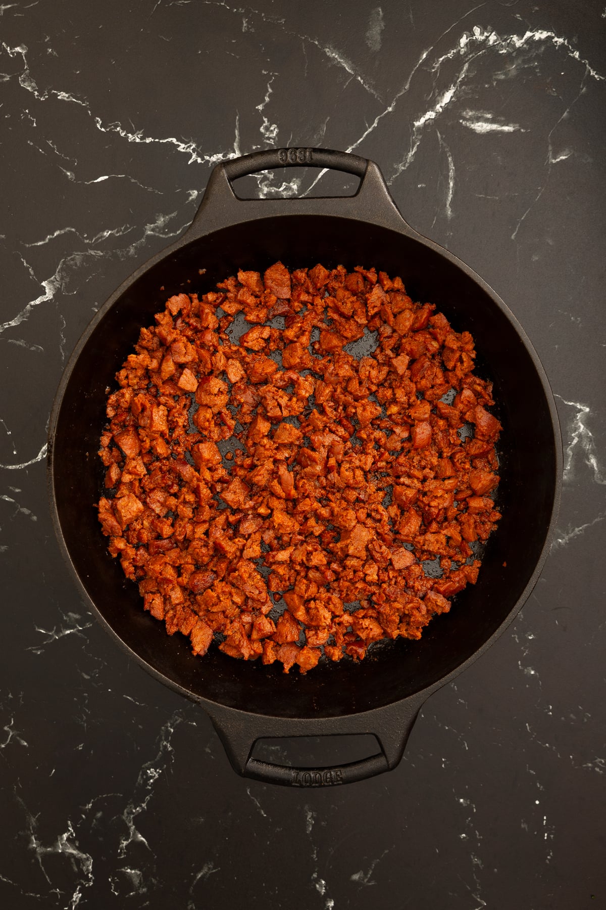 Cooked crumbled chorizo sausage in a black cast iron skillet on a dark marble countertop.