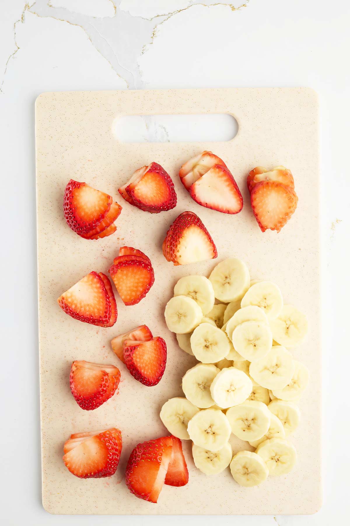Sliced strawberries and bananas arranged separately on a light-colored cutting board.