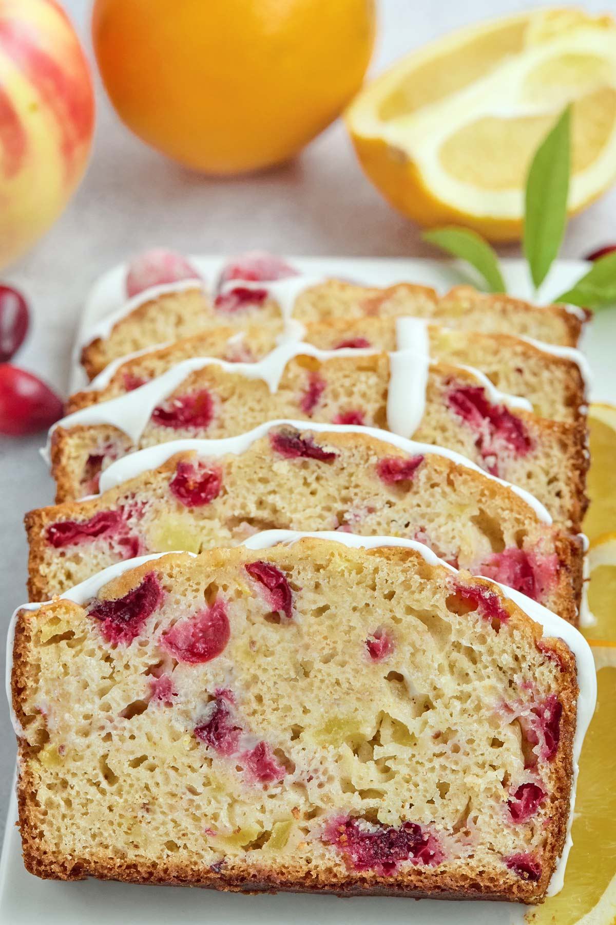 Sliced cranberry orange bread with white icing is arranged on a plate, alongside fresh oranges and cranberries—perfect for brunch, just like easy sheetpan pancakes.
