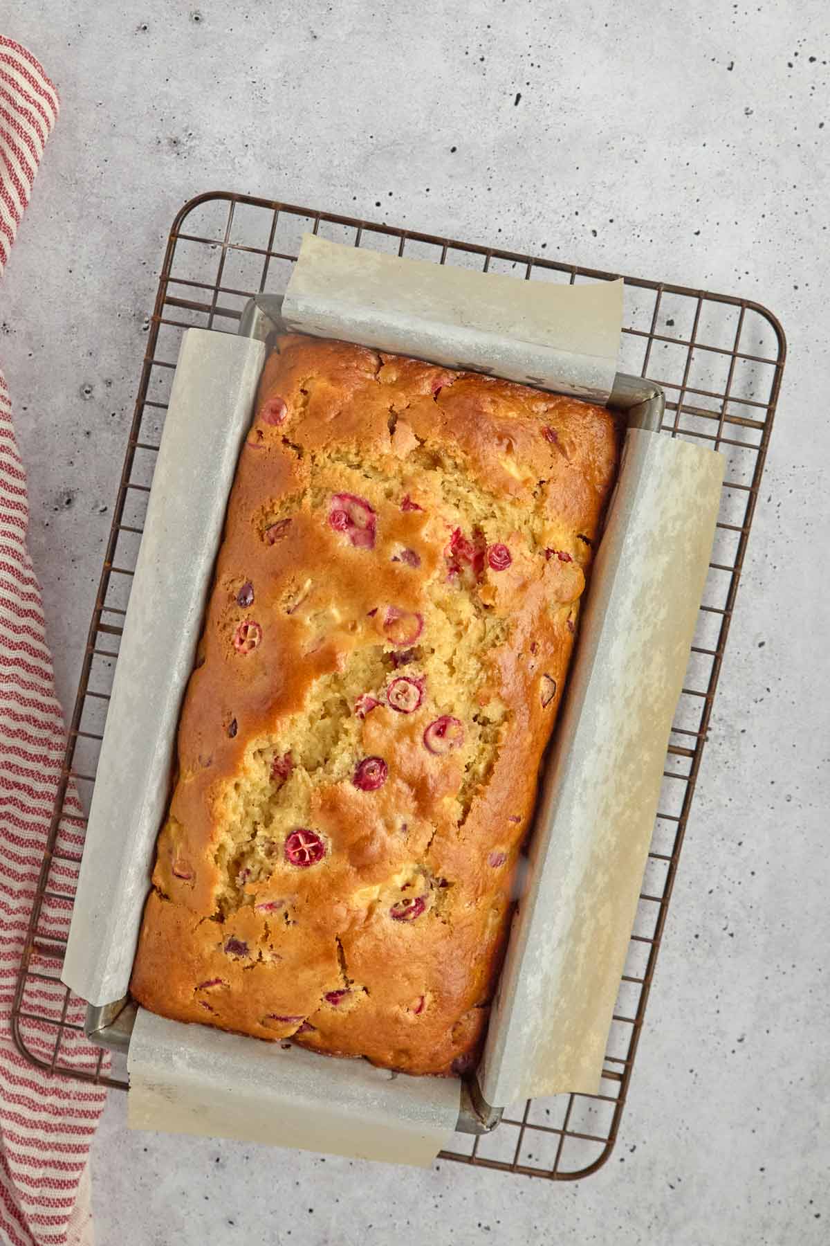 A loaf of cranberry bread in a parchment-lined baking pan on a wire cooling rack, viewed from above-perfect inspiration for your next easy sheetpan pancakes or favorite sheetpan pancake recipe.