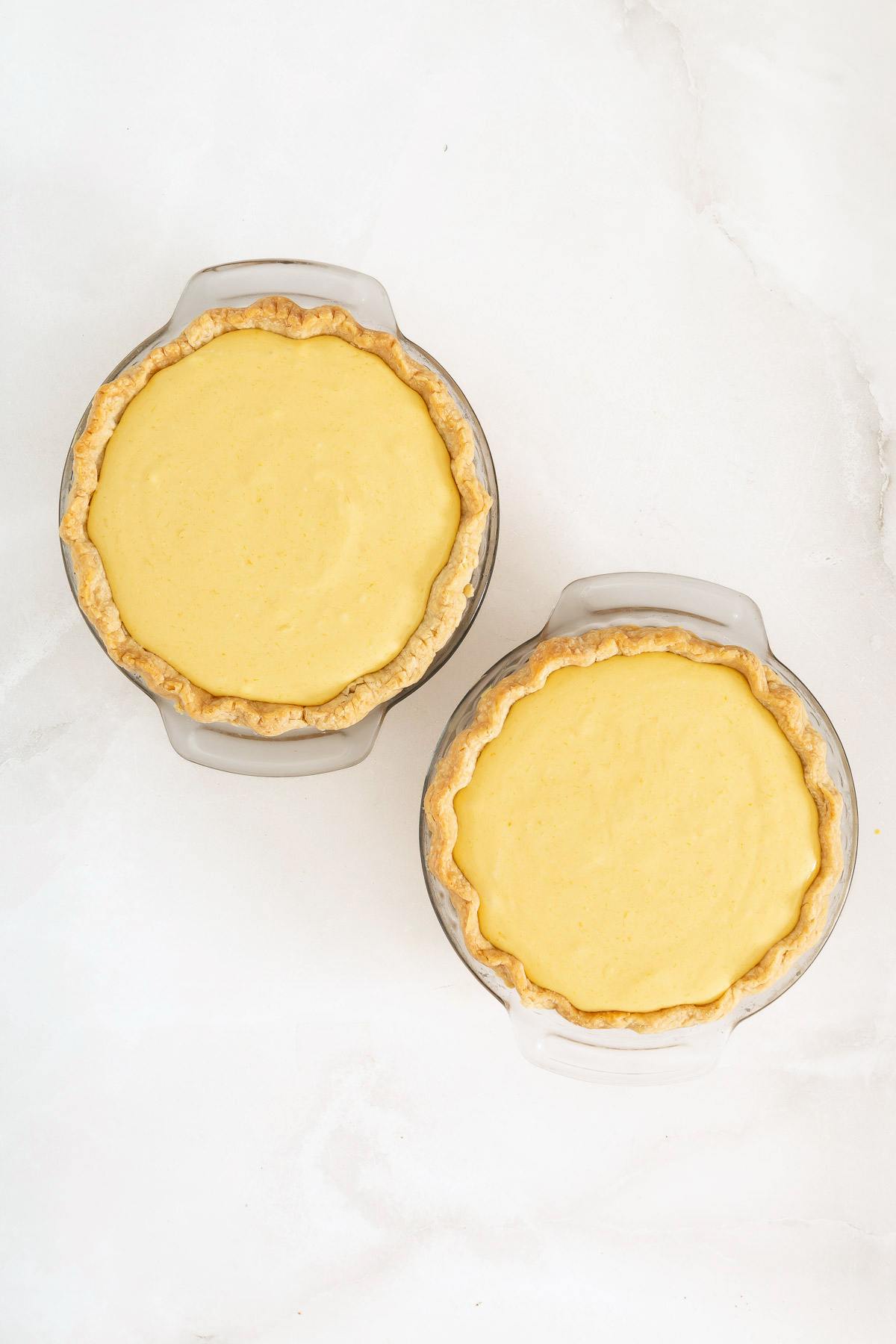 Two glass pie dishes each containing a baked Mango Pie with golden-brown crusts, placed on a white surface, ready to showcase your favorite mango pie recipe.