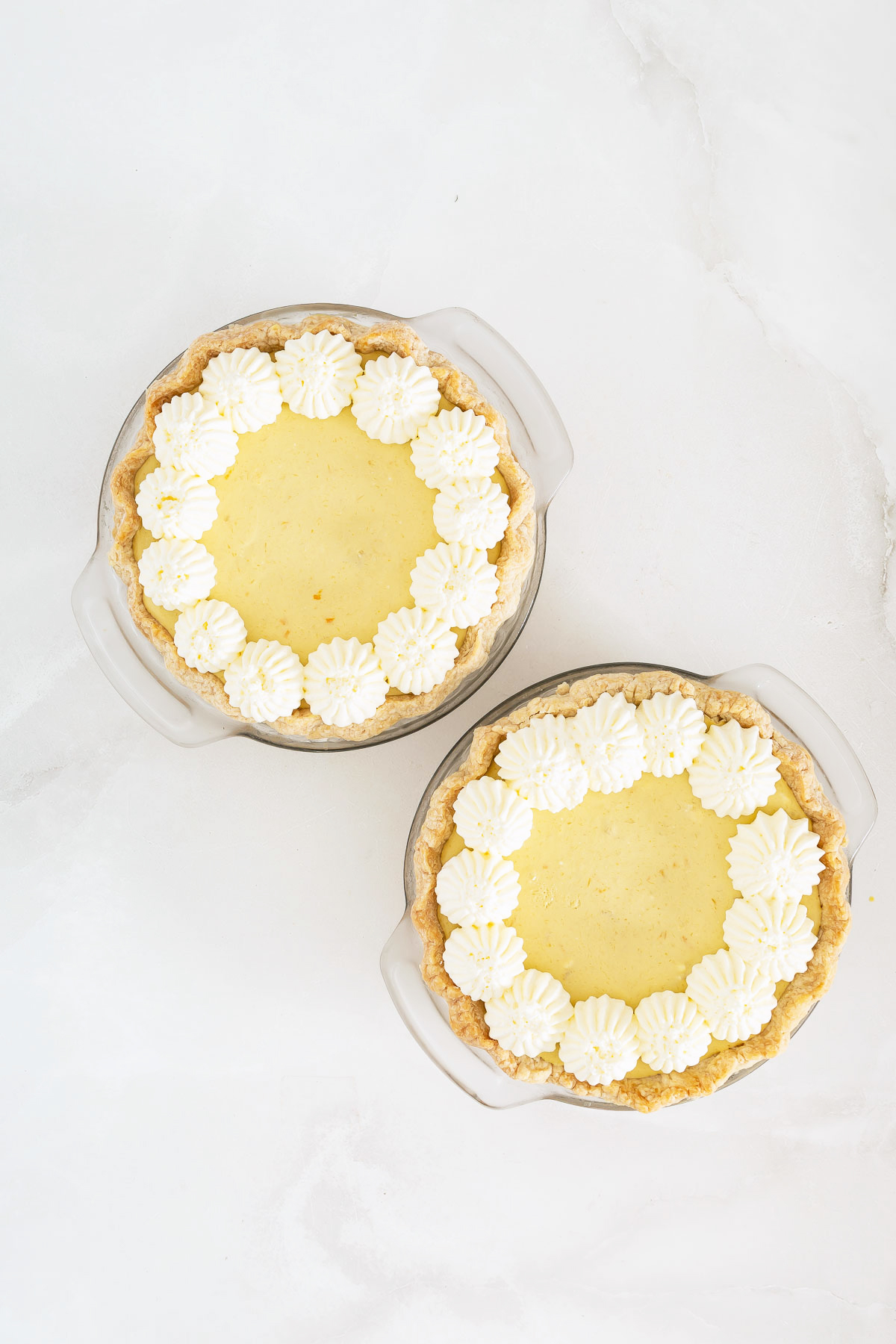 Two small, round mango fruit pies with flaky crusts and piped whipped cream decorations around the edges, placed on a white surface.