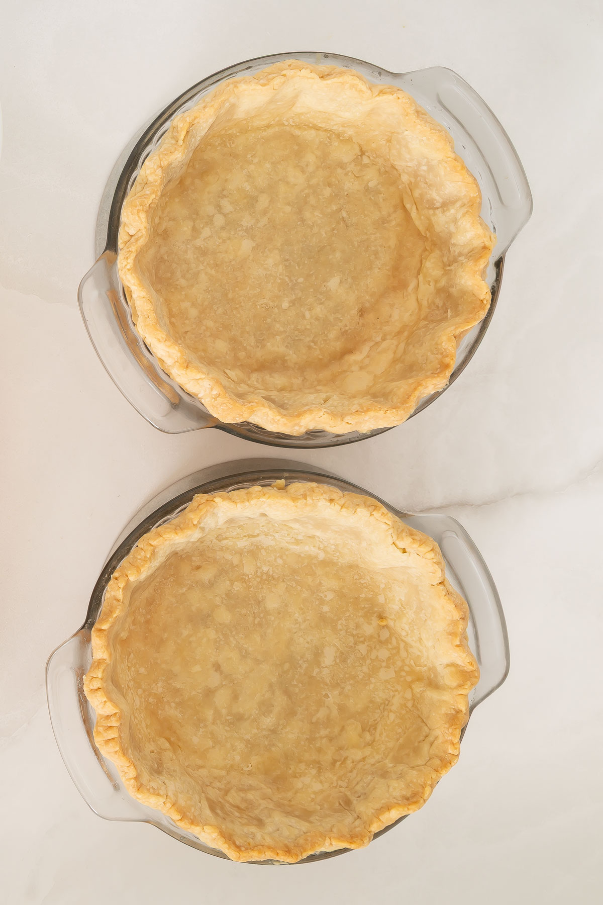 Two glass pie dishes with baked, empty pie crusts set on a white marble surface, ready for your favorite mango pie recipe.