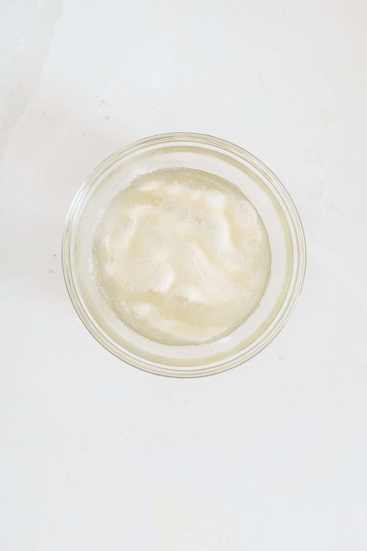 A small glass bowl filled with a white, granular powder on a plain white surface, perfect for creating the crust of your favorite mango pie recipe.