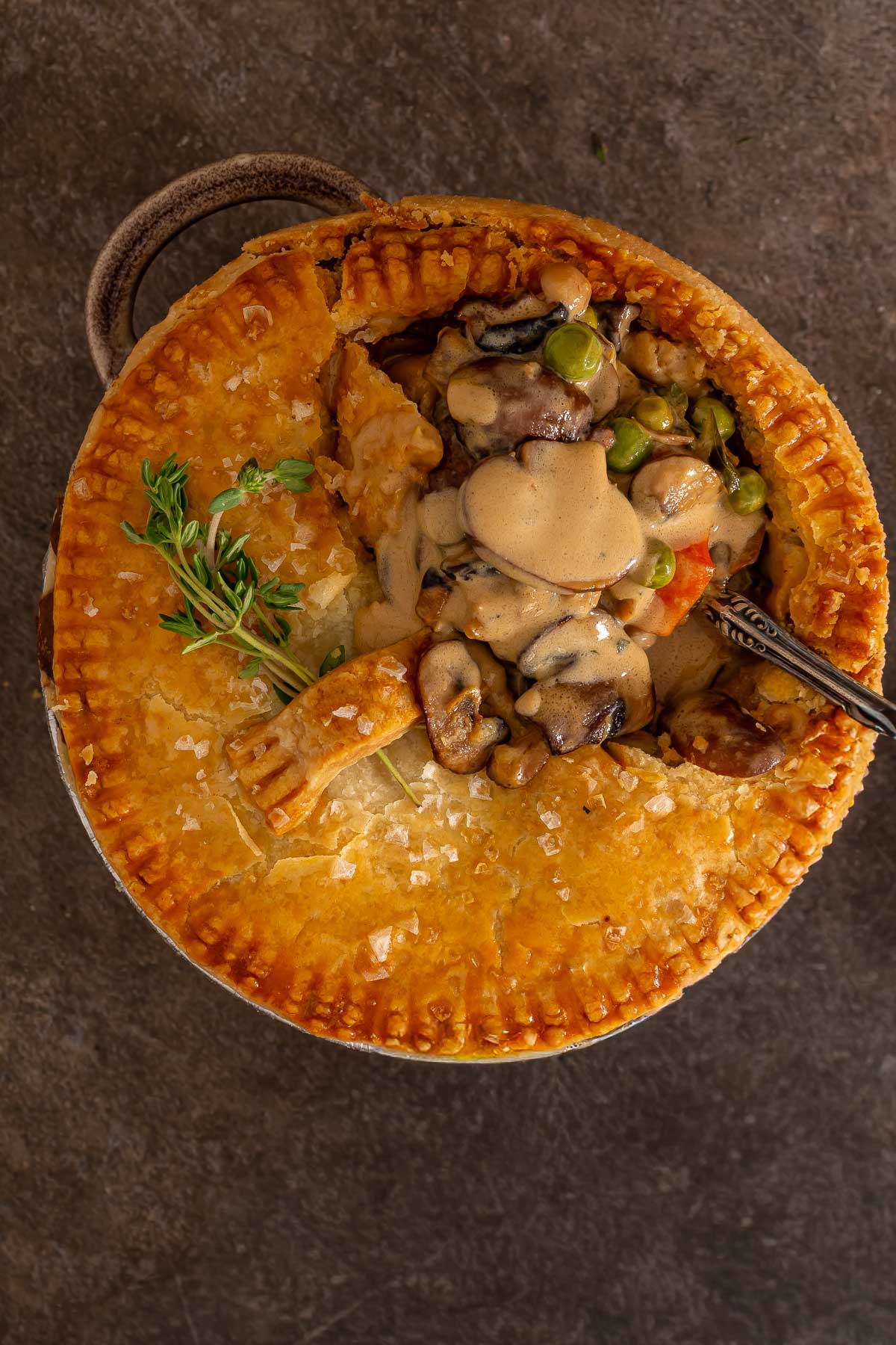 Golden-brown pot pie with a flaky crust, partially opened to reveal a creamy filling with mushrooms, peas, and vegetables; much like easy sheetpan pancakes, it's comfort food made simple. Sprigs of fresh herbs on top.
